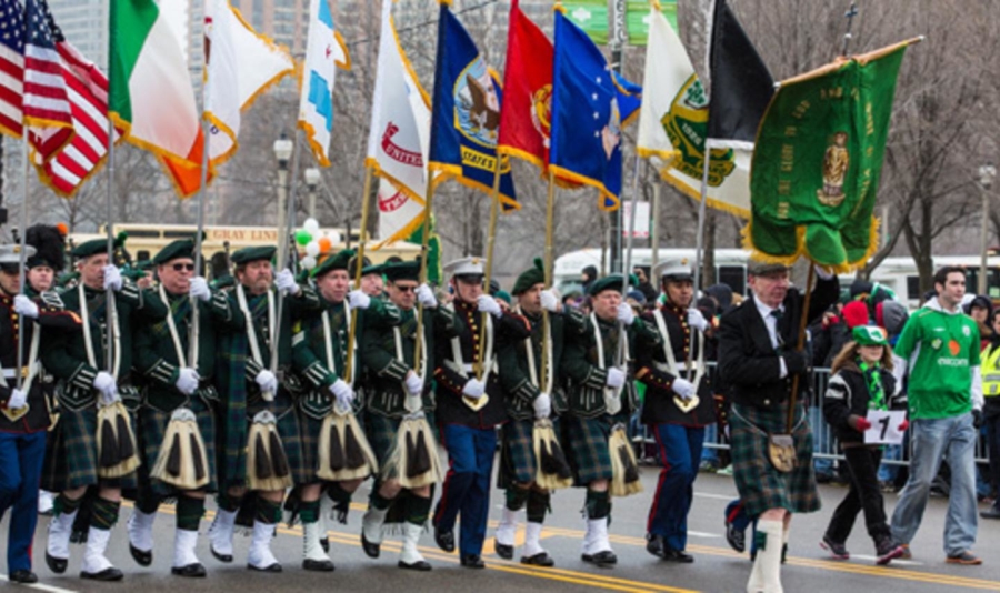 Parade members in kilts holding flags walk down the street in a group for the St Patricks Day Parade Chicago.
